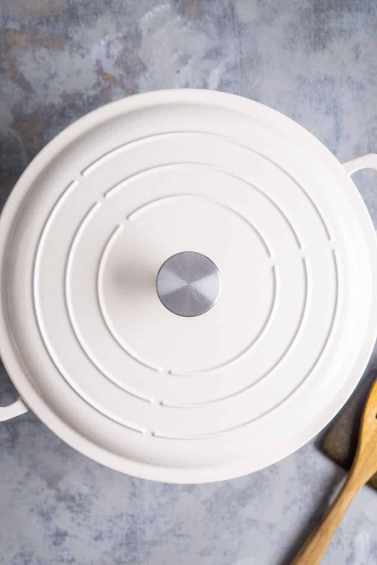 white lid sits on white pan next to wood stirring utensil