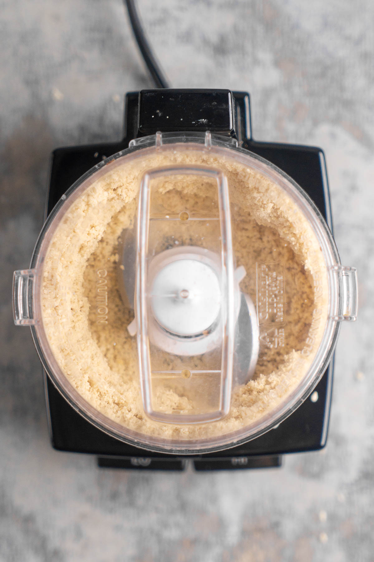 Top view of a food processor filled with white sesame seeds being processed.