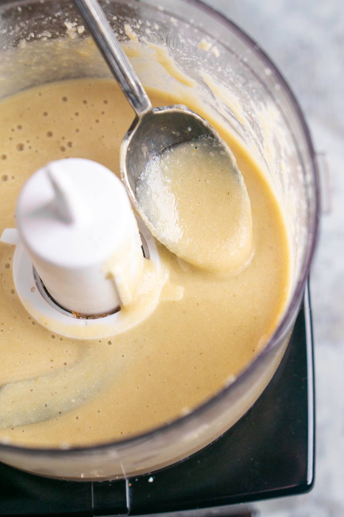A spoon rests in creamy tahini paste inside a food processor, showing the smooth consistency.
