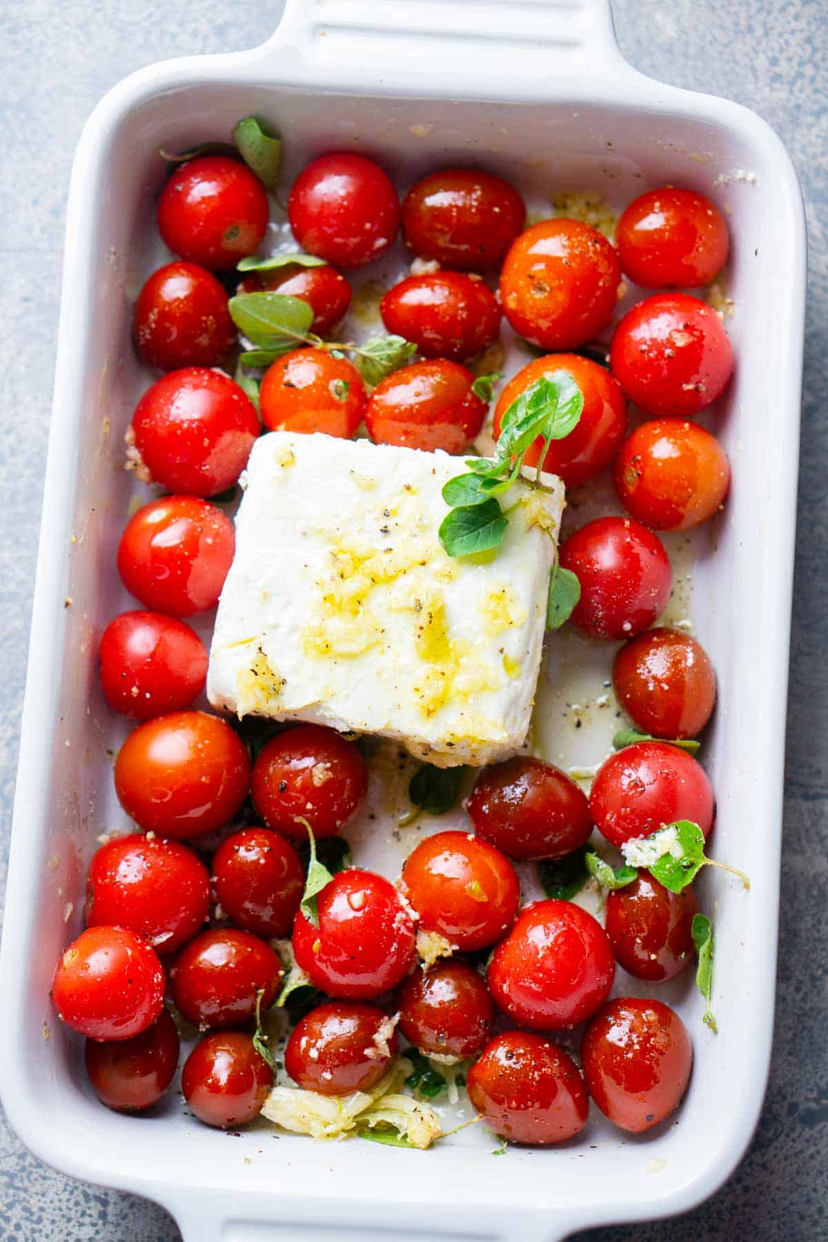 cherry tomatoes, feta cheese block, olive oil, and seasonings in white baking dish