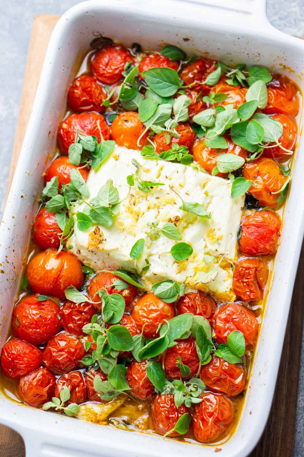 baked cherry tomatoes and baked feta topped with fresh oregano in white baking dish