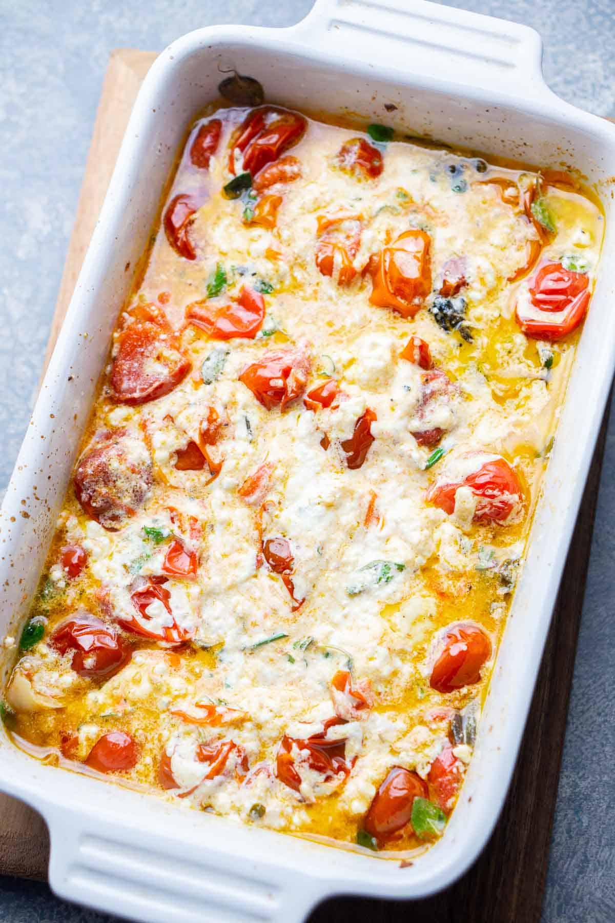 baked feta cheese and cherry tomatoes in white baking dish