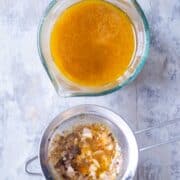turkey drippings in glass measuring cups next to mesh strainer with solids from turkey drippings