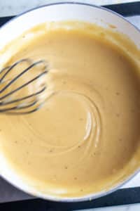 turkey gravy is being whisked by a black whisk in white saucepan