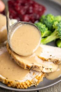 turkey gravy is ladled over sliced roasted turkey on a plate