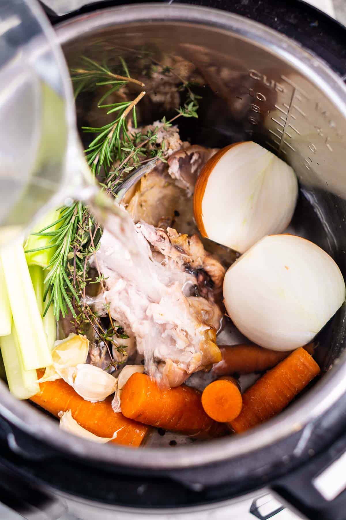water is added to a pot with turkey carcass, onions, carrots, and fresh herbs
