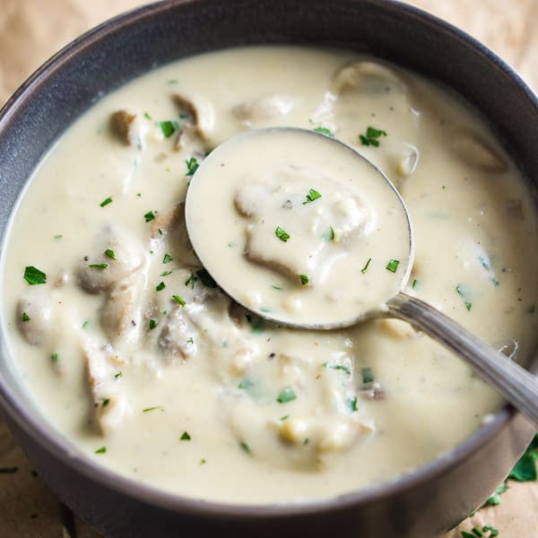 Soup spoon picks up vegan cream of mushroom soup from brown ceramic bowl on crinkled brown paper