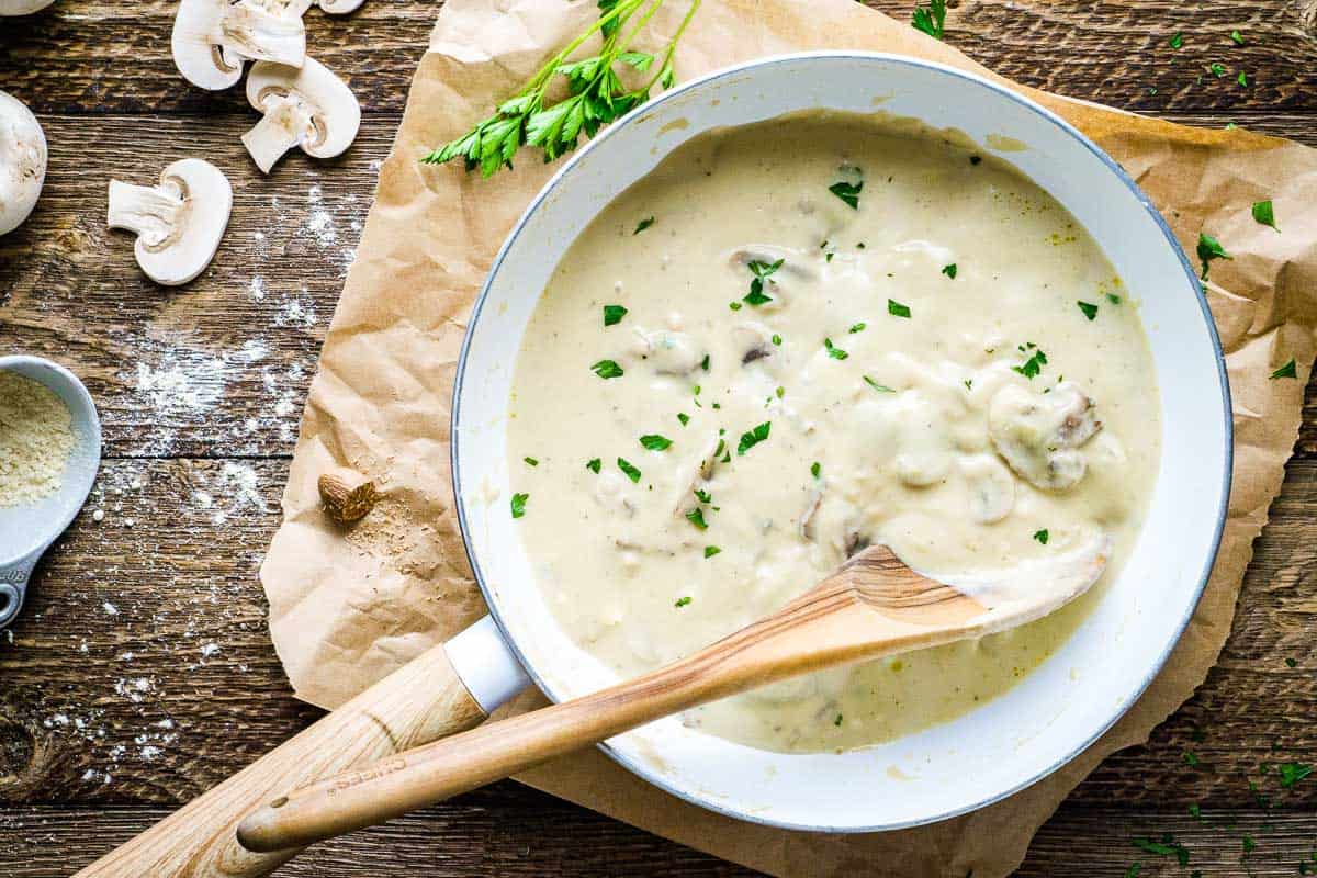 vegan cream of mushroom soup in white soup pot with wooden spoon