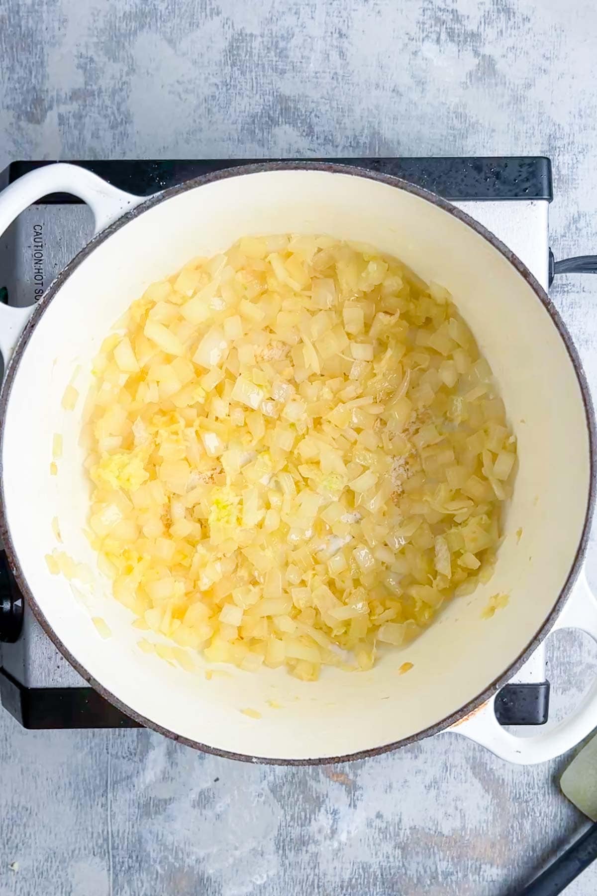 Chopped onions cooking in a white pot on a stovetop. The onions appear soft and slightly translucent.