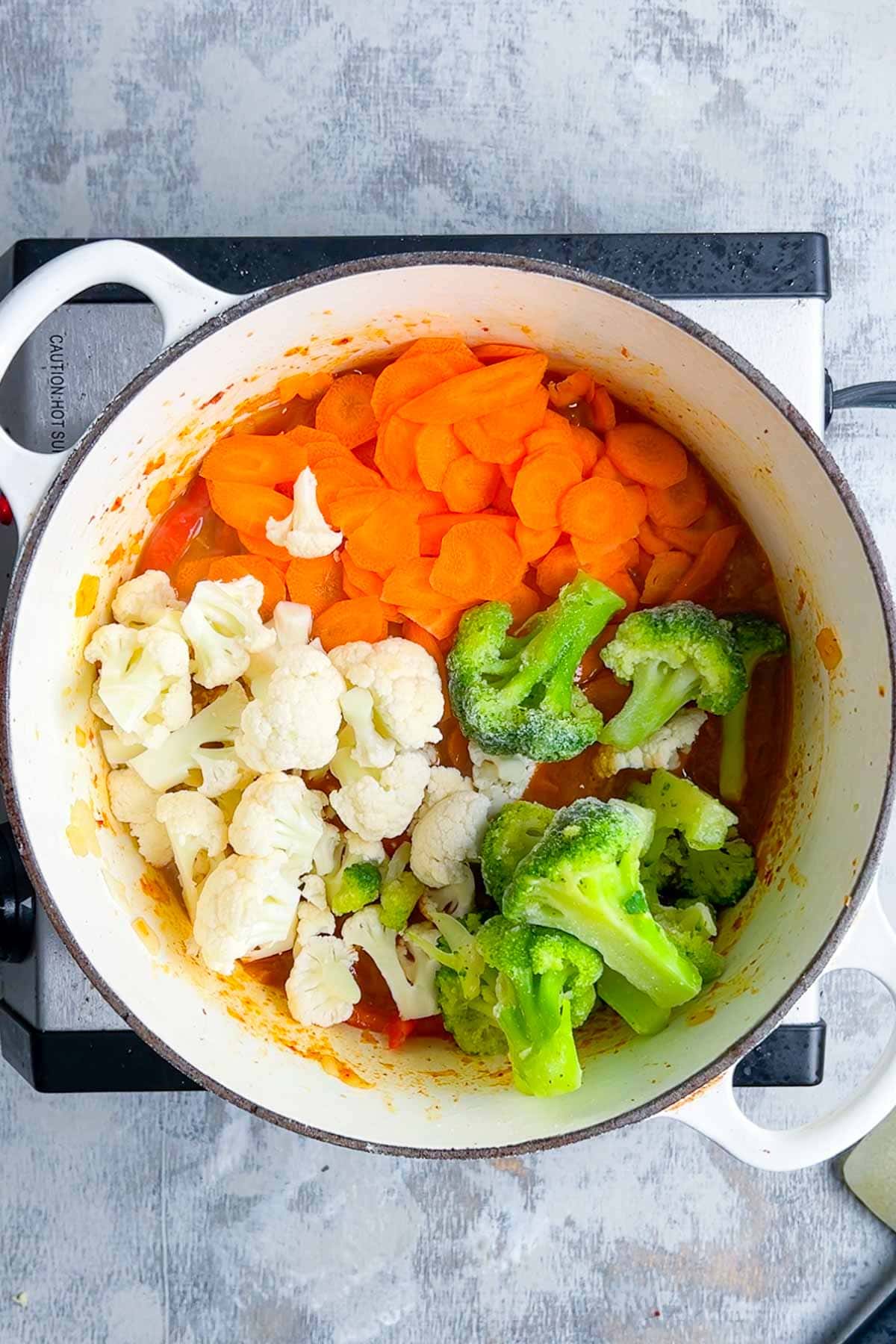 A pot on a stovetop contains sliced carrots, cauliflower, and broccoli.