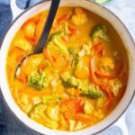 A pot filled with vibrant vegetable curry, featuring broccoli, carrots, red peppers, cauliflower, and a creamy red curry sauce.