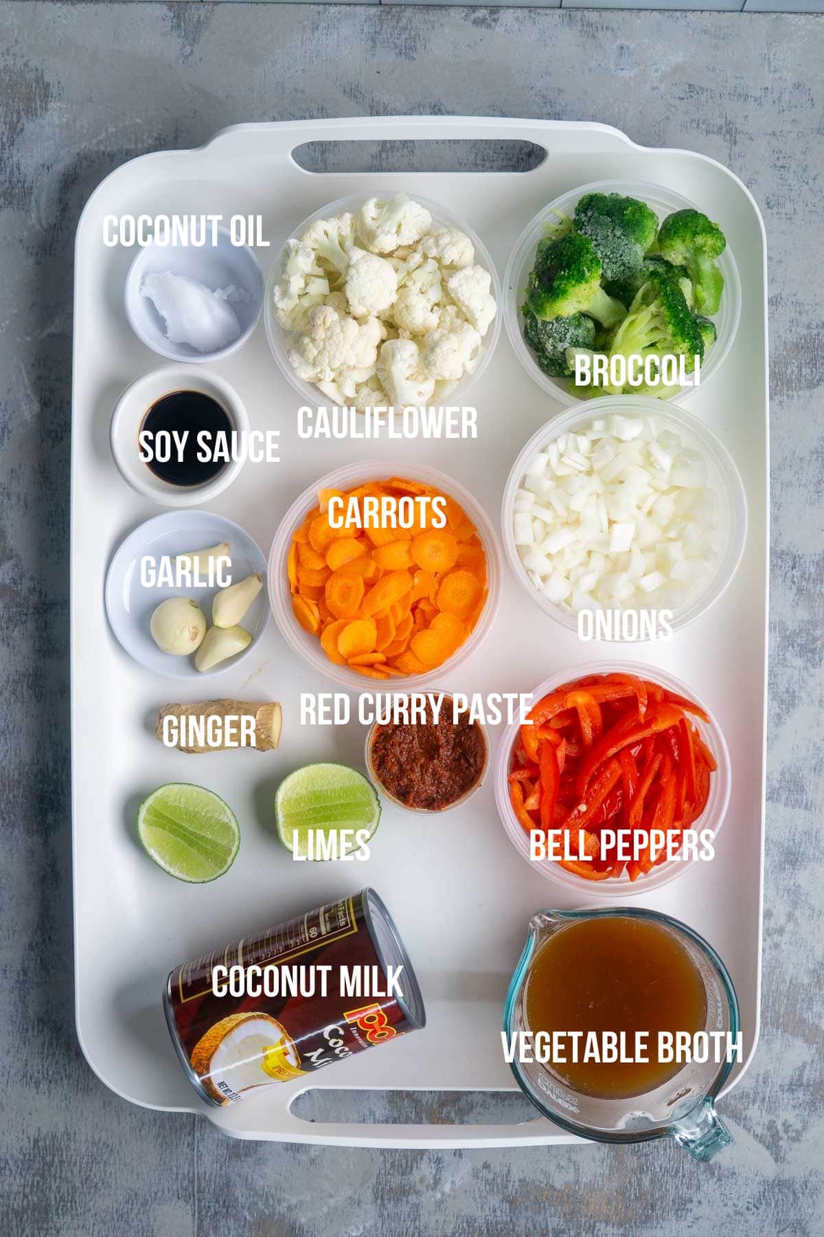 A tray with labeled ingredients: coconut oil, soy sauce, garlic, ginger, limes, coconut milk, cauliflower, carrots, red curry paste, onions, bell peppers, broccoli, and vegetable broth.