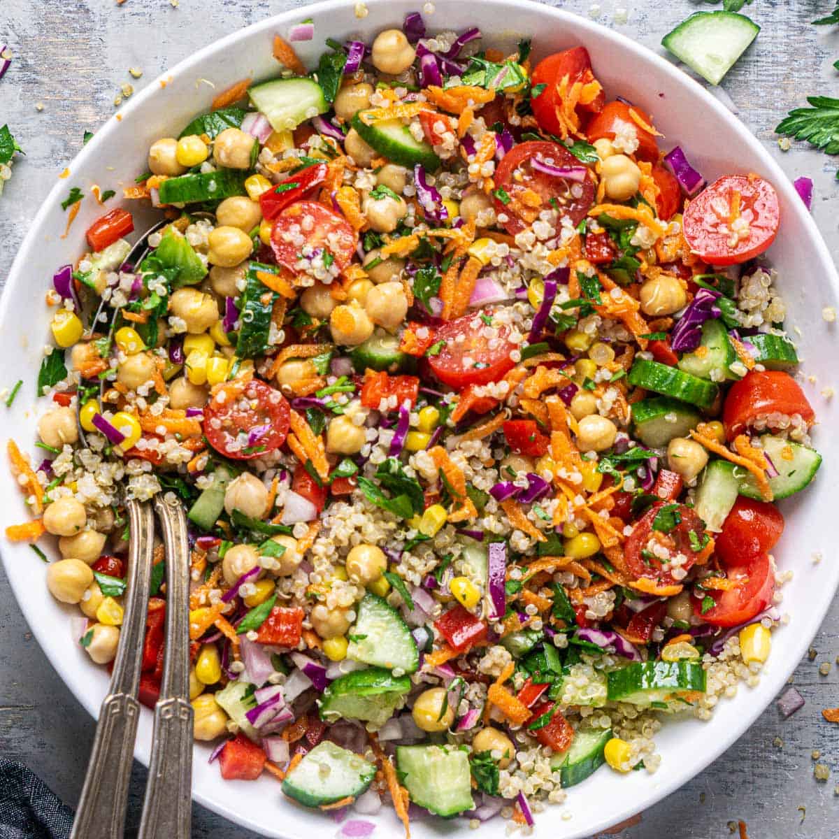 vegetable quinoa salad in white bowl with serving utensils