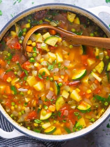 wooden ladle scooping up vegetable soup from a pot of vegetable soup