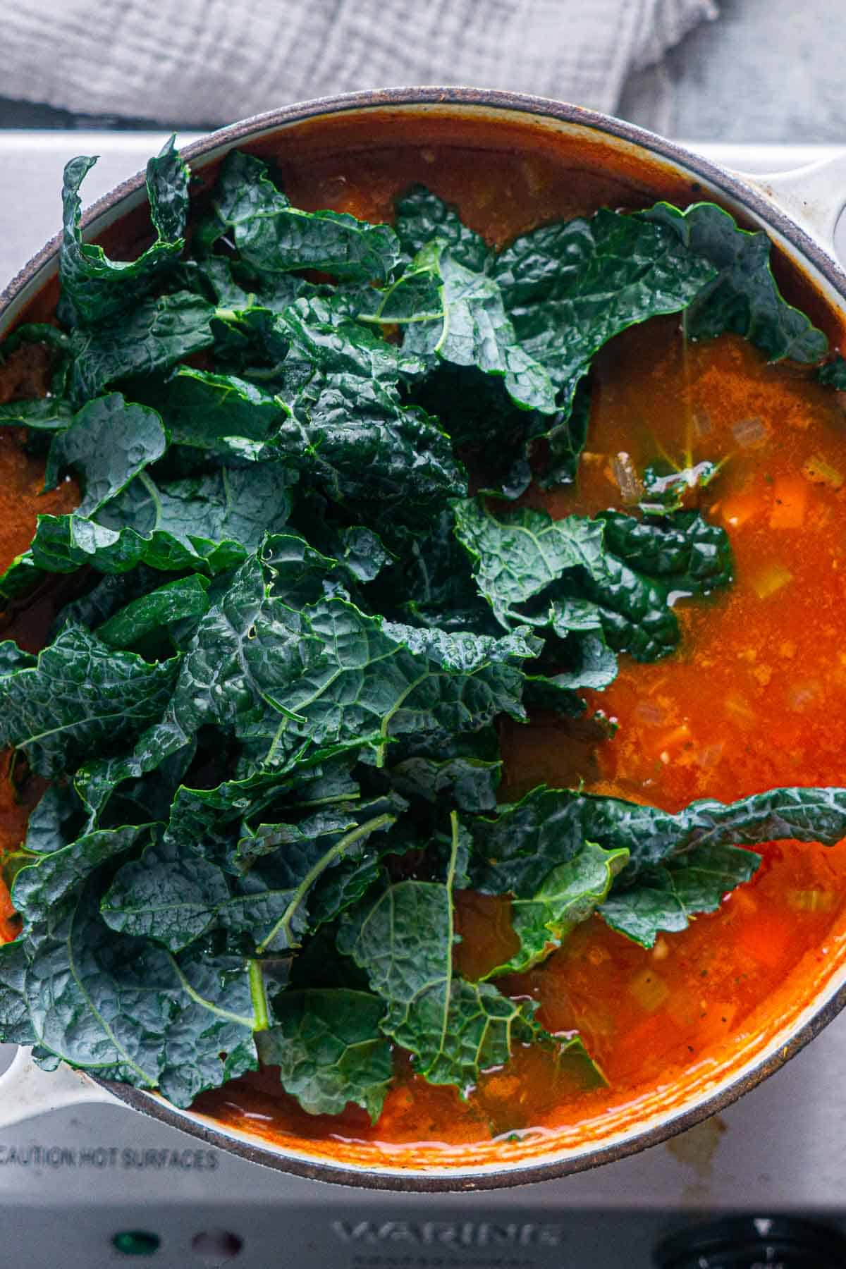 kale is piled on top of soup in dutch oven