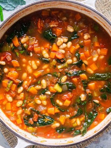 white bean kale soup in white dutch oven on burlap placemat