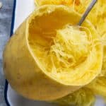 baked whole spaghetti squash is cut in half and fork is twirling noodle strands away from the shell